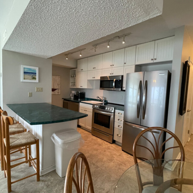 Modern kitchen with stainless steel appliances, green countertop, bar stools, and a glass dining table.