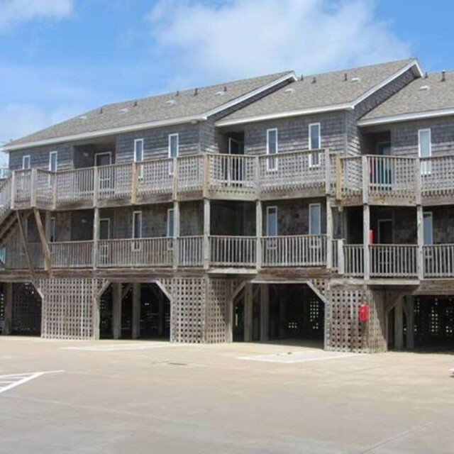 Two-story beach house with wooden exterior and balconies, elevated on stilts, parked van in foreground.