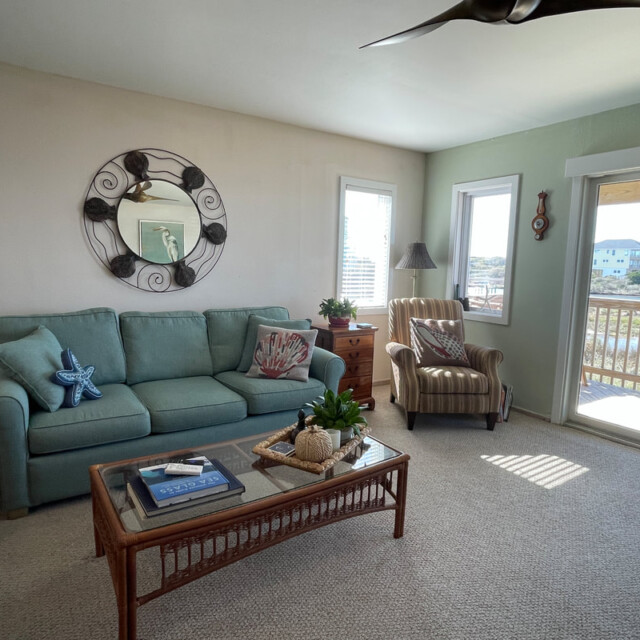 Living room with a blue sofa, striped armchair, coffee table, and sliding glass door leading to a balcony with a view.