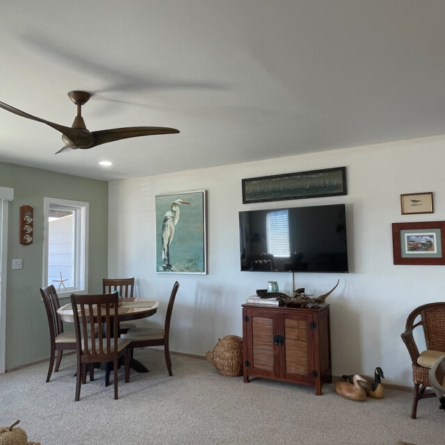 Living room with round dining table, wall art, a TV, wicker chairs, and sliding doors overlooking the ocean.