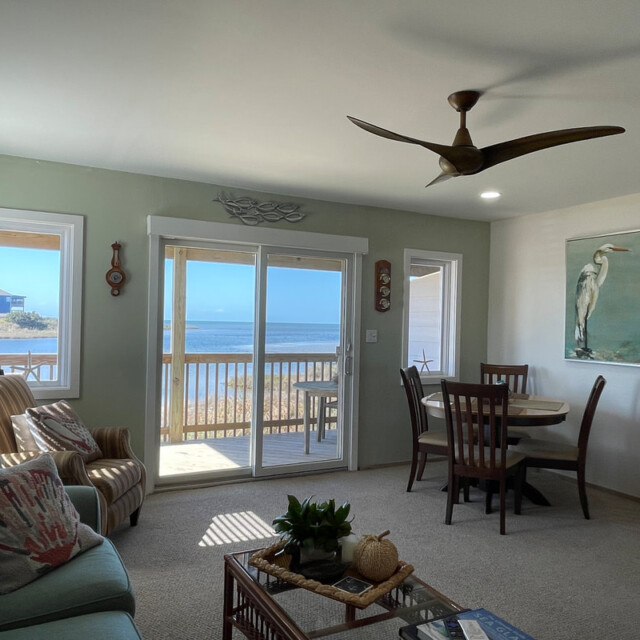 Living room with coastal decor, dining table, and sliding doors opening to a balcony with an ocean view.