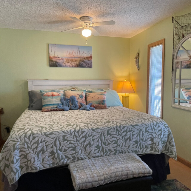 Bedroom with a king bed, beach-themed décor, bedside lamp, mirror, and light green walls.