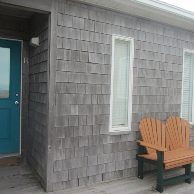 Wooden bench and two vertical windows next to a blue door on a shingled house exterior.