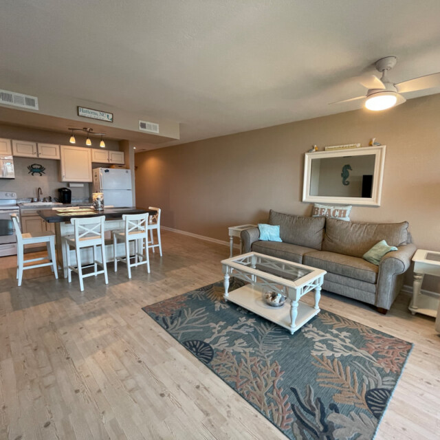 Open-plan living room and kitchen with neutral tones, beach-themed decor, and wooden flooring.