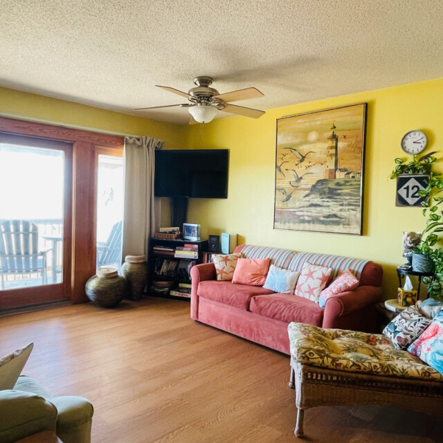 Bright living room with yellow walls, a red couch, wicker chaise, wall art, TV, and large glass doors to a balcony.