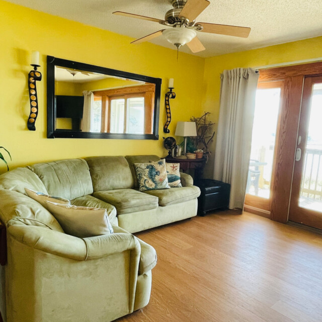 Living room with yellow walls, green sectional sofa, large mirror, ceiling fan, and glass doors to a balcony.