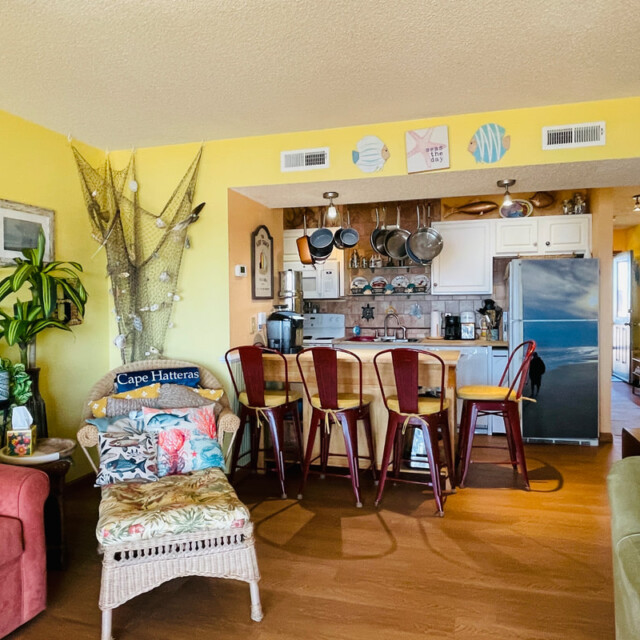 Colorful kitchen and living area with yellow walls, beach decor, bar stools, and various plants and wall art.