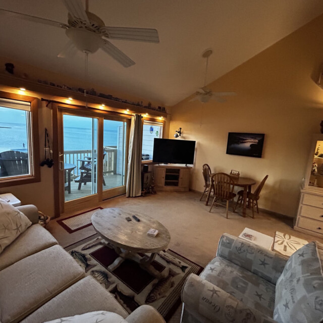 Living room with coastal decor, beige furniture, large windows, and a view of the ocean and a balcony outside.