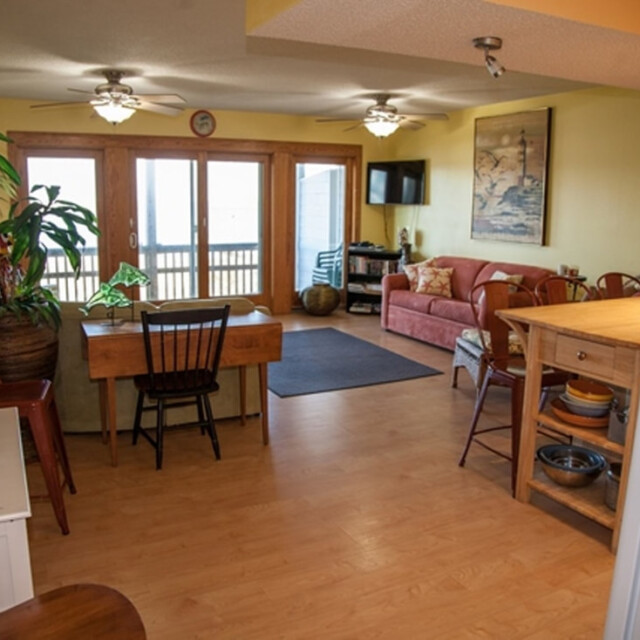 Open living area with wood floors, dining table, plants, sofa, wall art, and glass doors to a balcony.