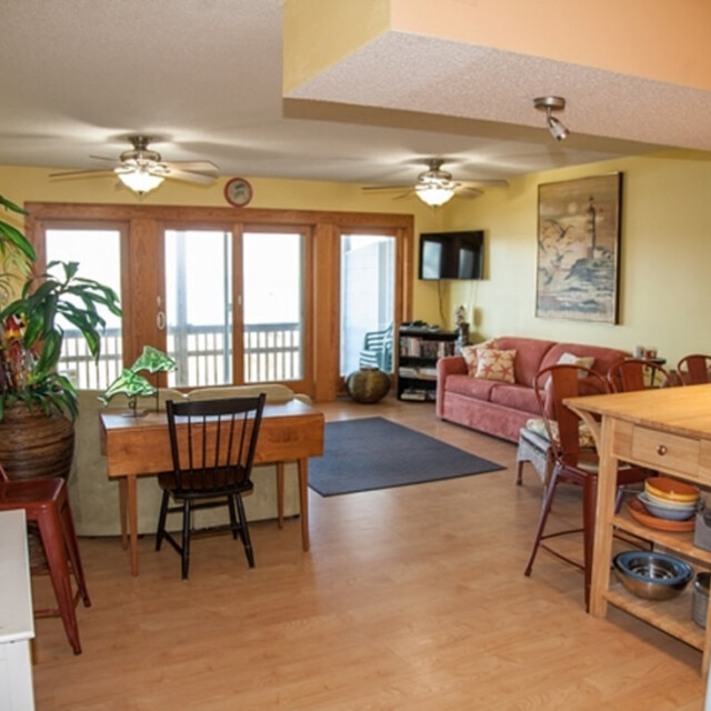 Open-plan living and dining area with yellow walls, wooden floors, and large windows leading to a balcony.
