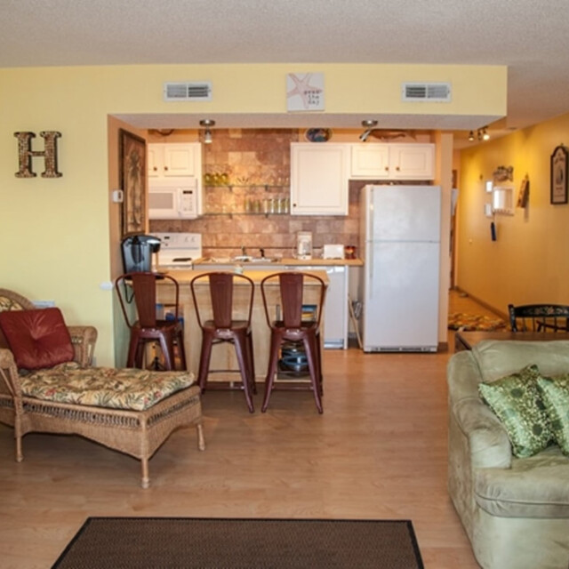 A small kitchen with bar stools, wicker furniture, and a light green couch in an open-plan living area.