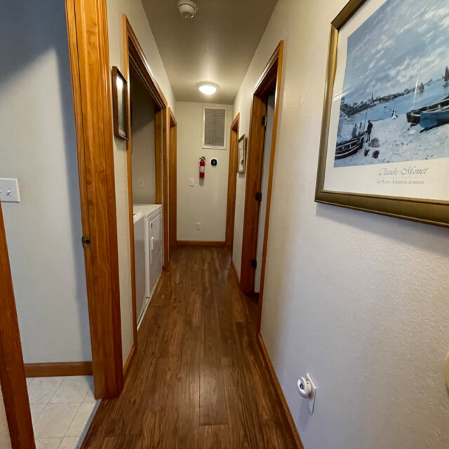 A hallway with wooden floors, open doorways, a laundry area, and a framed boating picture on the wall.