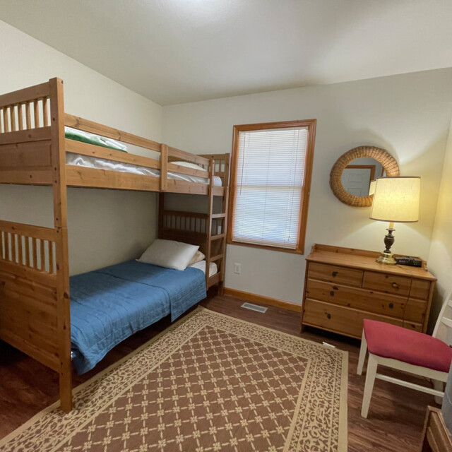 Bedroom with wooden bunk bed, dresser, mirror, lamp, chair, and rug on a hardwood floor.