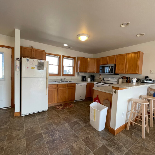 Spacious kitchen with wooden cabinets, white appliances, tiled floor, and a small breakfast bar with two stools.