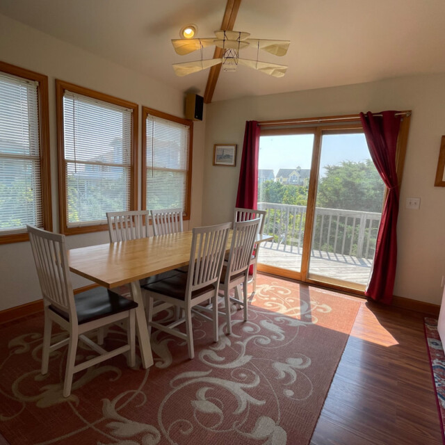 Dining area with a wooden table, six chairs, large windows, sliding glass door, and a balcony view.