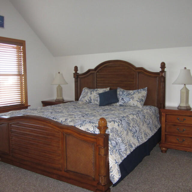 Bedroom with a large wooden bed, matching nightstands, two lamps, and windows with blinds on the left.