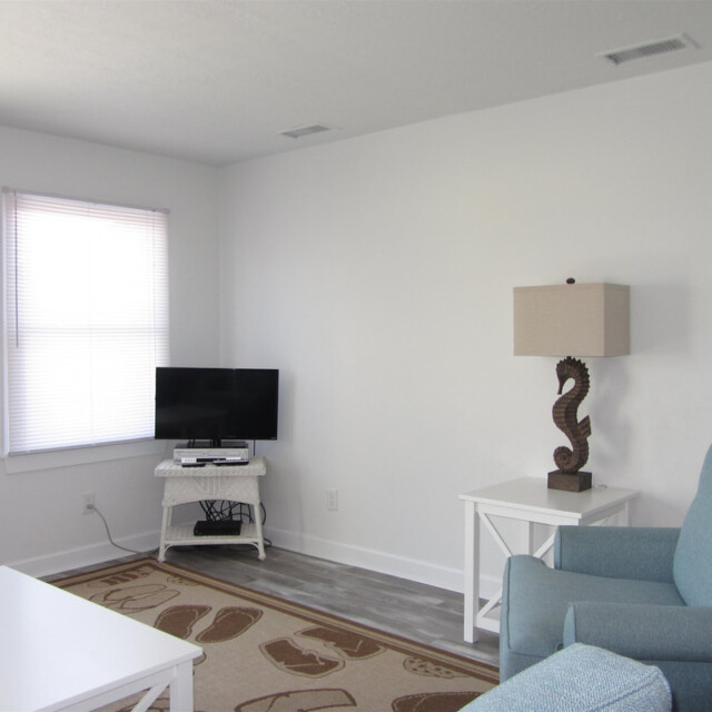 A living room with a blue armchair, small TV on a stand, seahorse lamp, and beach-themed decor.