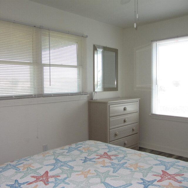 Bedroom with two windows, a dresser with a mirror, and a bed with a starfish-patterned bedspread.