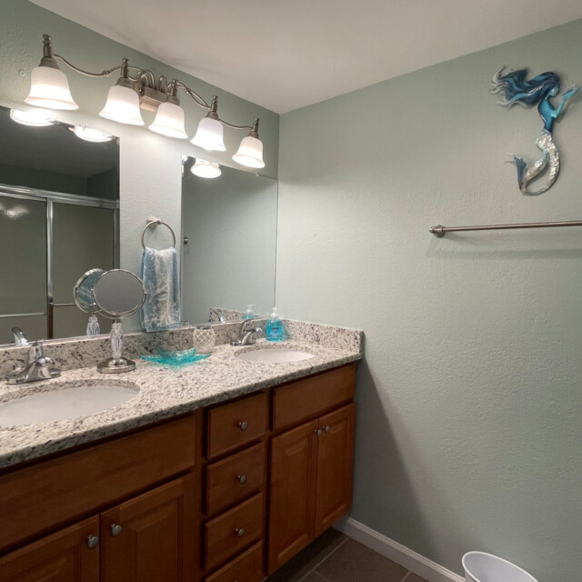 Bathroom with double sink vanity, granite countertop, mirror, lights, towel bar, and a mermaid wall decoration.