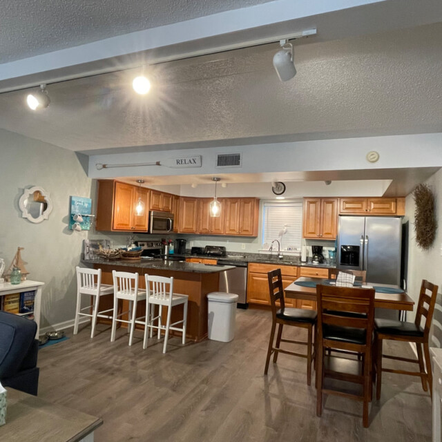 Open kitchen and dining area with wooden cabinets, stainless steel appliances, and seating for seven.