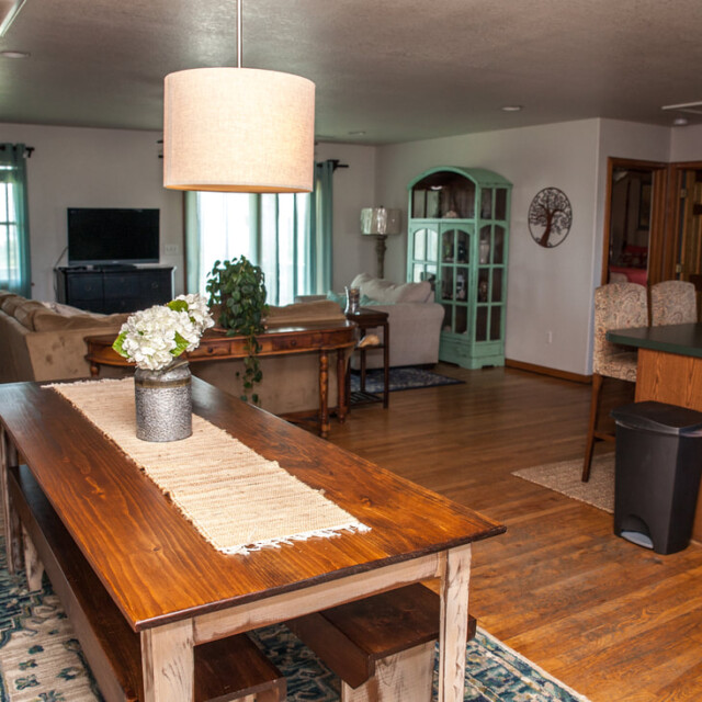 Open-concept living and dining area with wooden table, bench seating, and a sofa facing a TV.