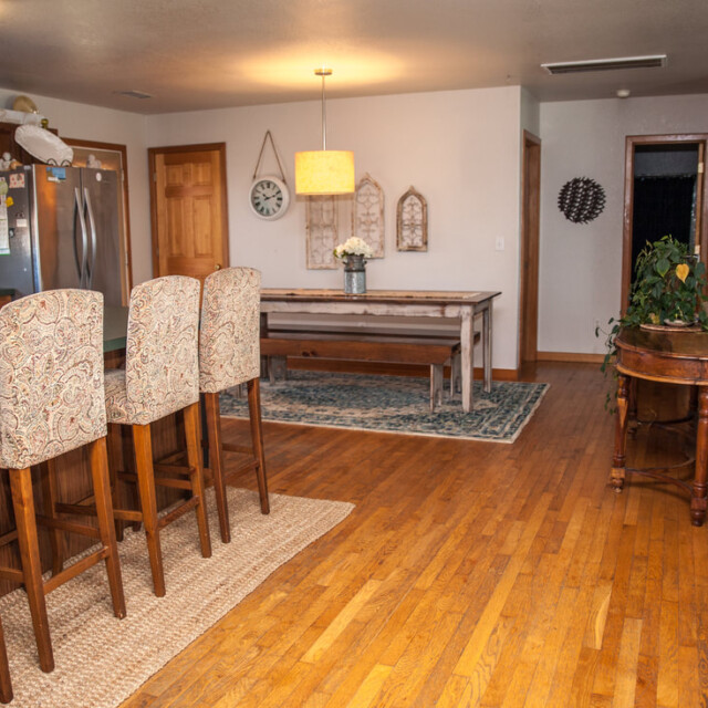 Open-plan kitchen and living room with wooden floors, an island with chairs, a dining table, and a couch.