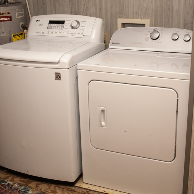 A white top-load washing machine and a front-load dryer side by side in a small laundry area with wood panel walls.