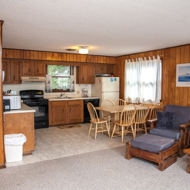 Kitchen and dining area in a wood-paneled room with a stove, fridge, table, chairs, and seating area.