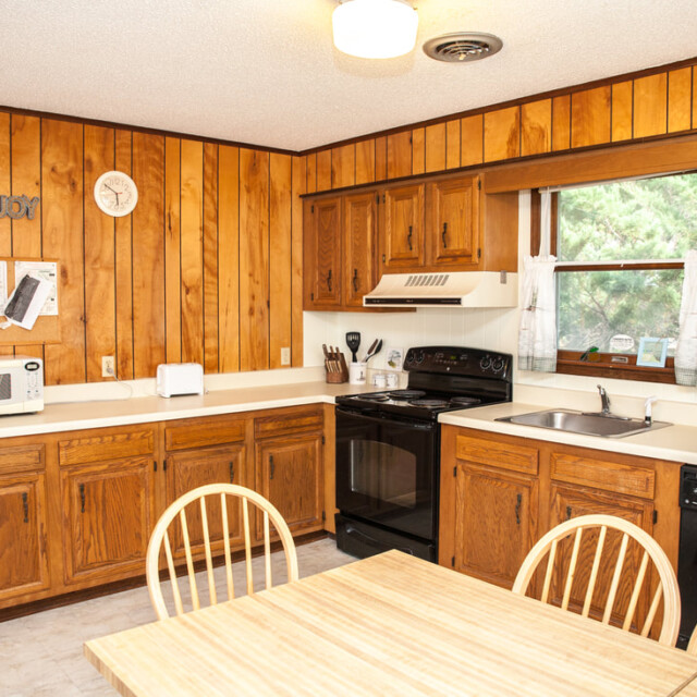 Kitchen with wood panel walls, wooden cabinets, black appliances, a microwave, and a dining table with four chairs.