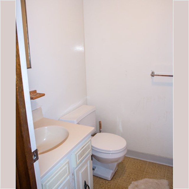 Small bathroom with white walls, a sink vanity, toilet, towel rack, and a towel on the beige patterned floor.