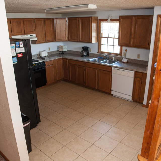 L-shaped kitchen with wooden cabinets, black refrigerator, stove, dishwasher, and tiled floor, viewed from above.