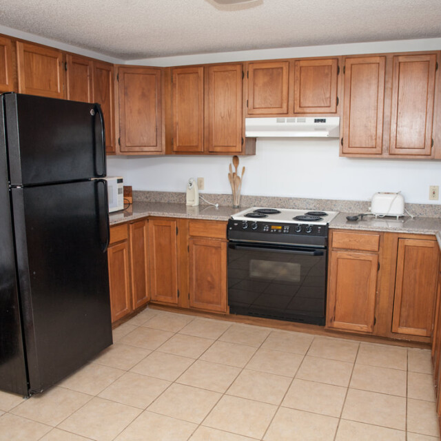 Kitchen with wood cabinets, black fridge and stove, beige countertops, sink, and tiled floor.