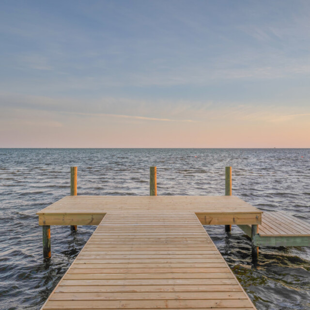 A wooden dock extends over calm water under a clear sky at sunset.