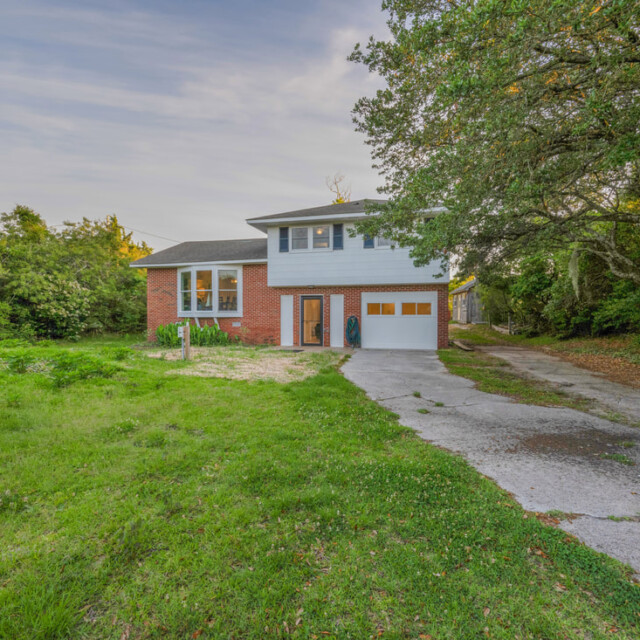 Two-story house with a brick and white exterior, surrounded by trees and a large grassy yard with a driveway.