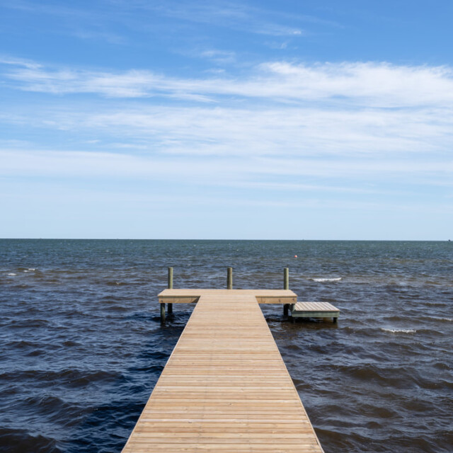 Wooden dock extends over choppy water under a blue sky with scattered clouds.