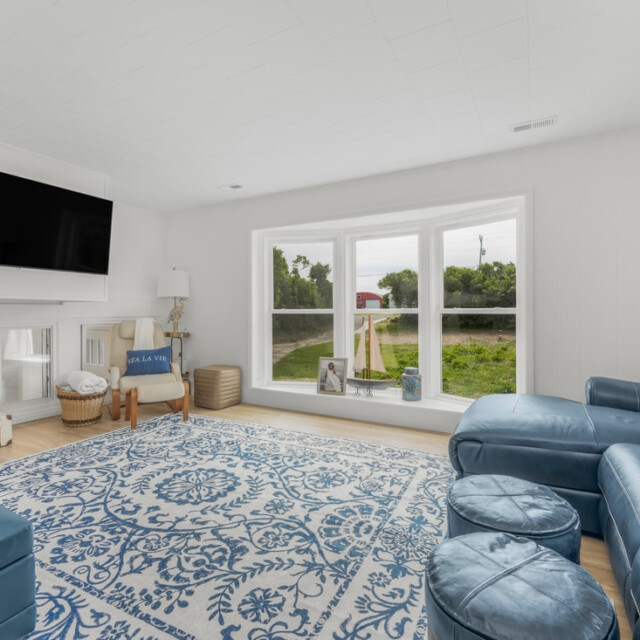 Living room with blue sectional sofa, patterned rug, large windows, and a wall-mounted TV next to wooden stairs.