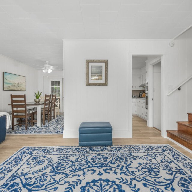 Bright living room with blue and white decor, wooden stairs, and a view into the dining area and kitchen.