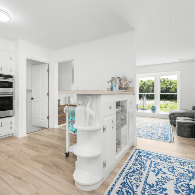Bright kitchen with white cabinets, a center island, and a view into a living area with large windows and blue accents.