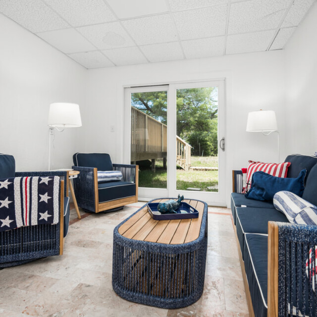 Patriotic-themed sitting room with blue wicker furniture, striped and star pillows, and a sliding glass door to the outside.