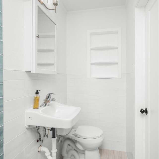 Small bathroom with a white sink, toilet, wall cabinet, shelves, and blue tile accent walls.