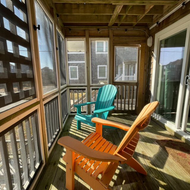 Two Adirondack chairs sit on a screened porch with wooden floors, sunlight streaming through the windows.