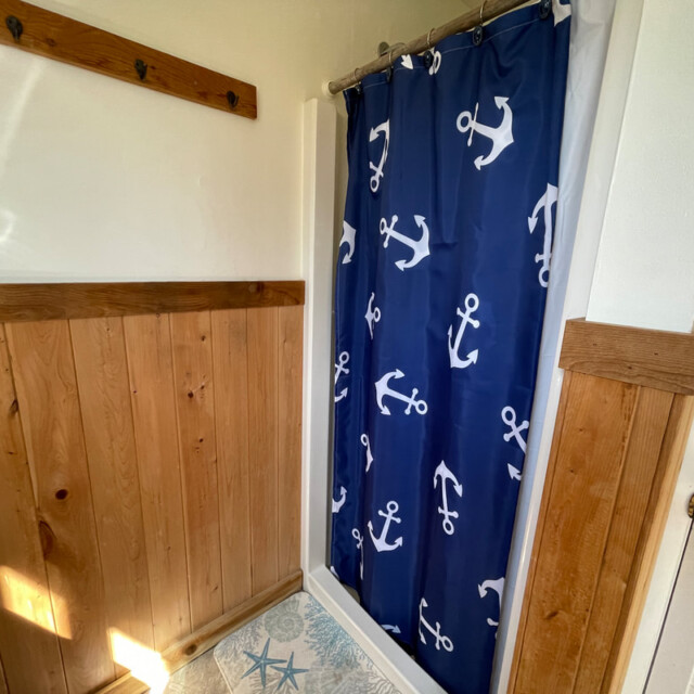 Small shower with a blue anchor-patterned curtain, wood paneling on the walls, and nautical-themed tile floor.