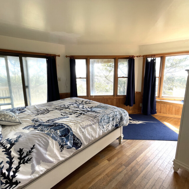 Bright bedroom with large windows, wooden floors, a bed with blue floral bedding, and dark blue curtains.