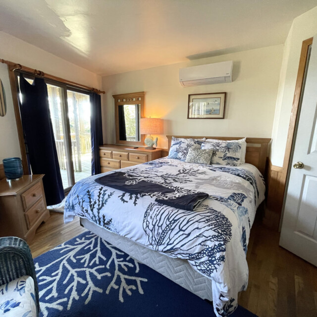 Bedroom with a double bed, dresser, mirror, and sliding glass doors leading to a deck, decorated in a coastal theme.
