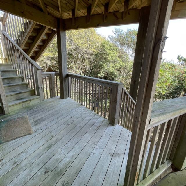Wooden deck with railing, stairs leading up and down, and trees visible beyond the railings on a sunny day.
