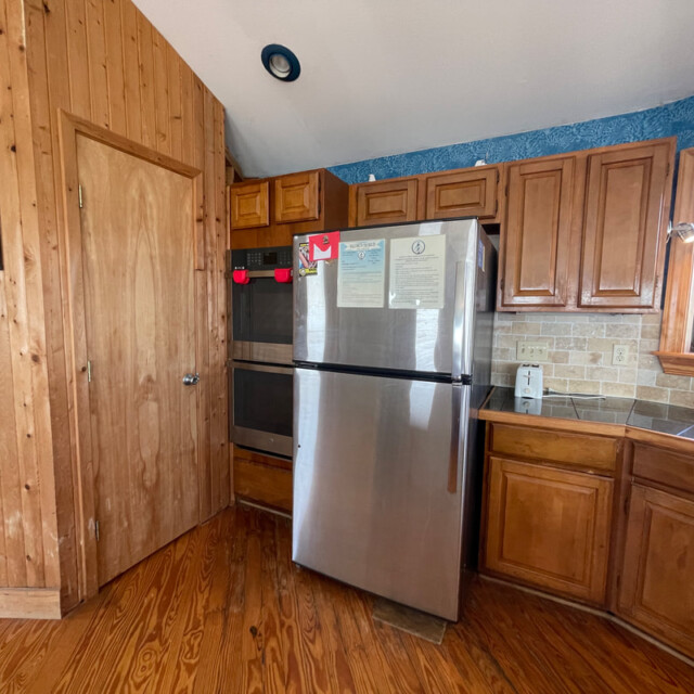 Kitchen with wood cabinets, stainless steel fridge, double oven, and window above the counter on the right.