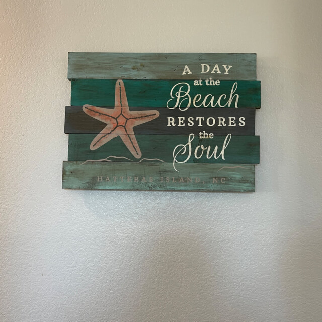 Wooden wall sign with a starfish and the words “A day at the beach restores the soul. Hatteras Island, NC.”.