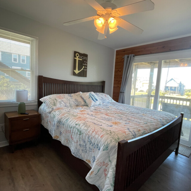 Bedroom with a wooden bed, floral quilt, nightstand, ceiling fan, and sliding glass doors to a porch.