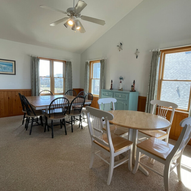 Dining room with two tables, chairs, a ceiling fan, large windows, and a light blue cabinet along the wall.