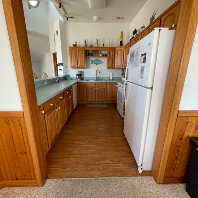 A small kitchen with wooden cabinets, white appliances, green countertops, and decorative items on upper shelves.